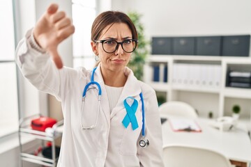 Wall Mural - Young brunette doctor woman wearing stethoscope at the clinic looking unhappy and angry showing rejection and negative with thumbs down gesture. bad expression.