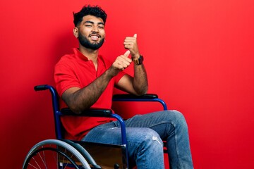 Poster - Arab man with beard sitting on wheelchair pointing to the back behind with hand and thumbs up, smiling confident