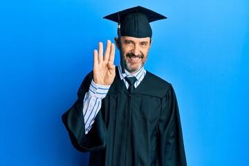 Poster - Middle age hispanic man wearing graduation cap and ceremony robe showing and pointing up with fingers number four while smiling confident and happy.