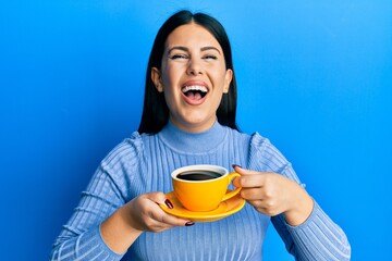 Poster - Beautiful brunette woman drinking a yellow cup of black coffee smiling and laughing hard out loud because funny crazy joke.