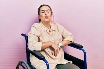 Sticker - Young hispanic woman sitting on wheelchair looking at the camera blowing a kiss on air being lovely and sexy. love expression.