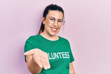 Poster - Young hispanic woman wearing volunteer t shirt smiling cheerful offering palm hand giving assistance and acceptance.