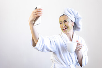 Canvas Print - Young woman with a green beauty mask on her face with a cup and a smartphone.