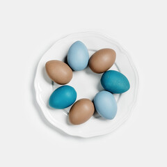 Wall Mural - Dyed Easter eggs pastel colors blue, beige on round white plate. Happy Easter holiday concept, celebration food, decorated chicken egg, neutral trendy colored card. Top view table