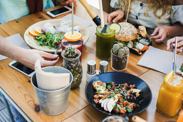 Hands view of young people eating brunch and drinking smoothies in healthy bar restaurant - Focus on left hand