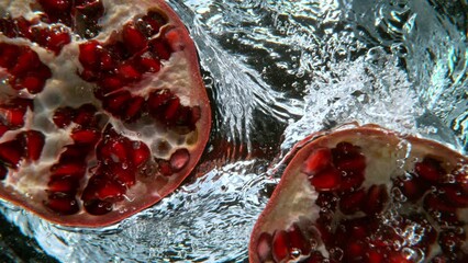 Wall Mural - Fresh sliced pomegranate falling into water, super slow motion filmed on high speed cinematic camera at 1000 fps.