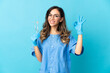 © luismolinero - Woman dentist holding tools over isolated on blue background showing ok sign with fingers