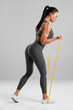 © nikolas_jkd - Fitness woman doing exercise with resistance band on gray background. Athletic girl working out