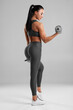 © nikolas_jkd - Beautiful fitness woman with dumbbells. Athletic girl on the gray background