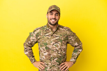 Wall Mural - Military man isolated on yellow background posing with arms at hip and smiling