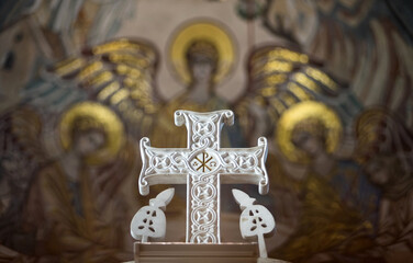 Beautiful white carved marble Orthodox cross on the background of a mosaic panel