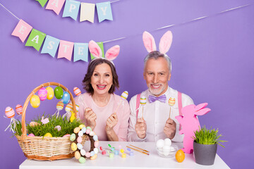 Poster - Photo of funny positive people hold craft eggs stick enjoy festive isolated on purple color background