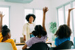 Primary African American school boy and girls raising hands up to ask a teacher questions in classroom. Education concept
