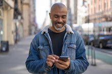 Mature Black Man In City Using Cell Phone Walking On A Street
