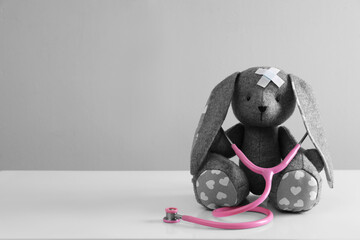 Toy bunny with stethoscope on white table against light grey background, space for text. Children's hospital