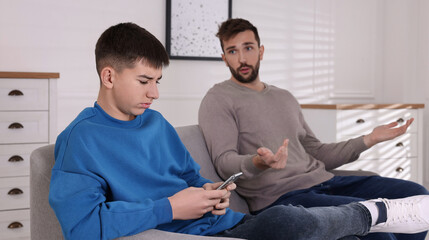 Wall Mural - Boy using smartphone and ignoring his upset father at home. Teenager problems