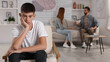 © New Africa - Unhappy teenage boy sitting in armchair while his parents arguing on background. Problems at home