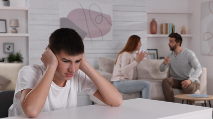 Unhappy teenage boy covering ears while his parents arguing on background. Problems at home