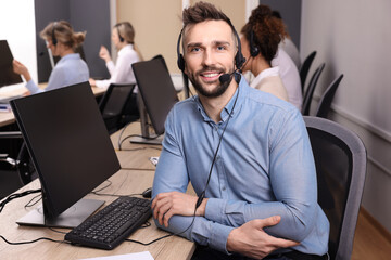 Wall Mural - Call center operator with headset and his colleagues working in modern office