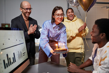 Diverse group of colleagues applauding while bringing surprise Birthday cake to smiling young man in office