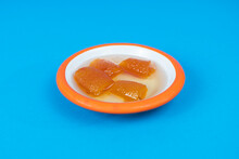 Close-up Shot Of Orange Jam And White Plate With Orange Rim On Isolated Area, Blue Background From Opposite Or Side Angle With Selective Focus.