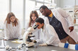 © Seventyfour - Side view portrait of young black girl looking into microscope with while doing experiments with group of children in school chemistry lab, copy space