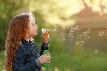 Sticker - Curly girl blowing soap bubbles in summer park.