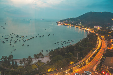 Vung Tau city aerial view with beautiful sunset and so many boats. Panoramic coastal Vung Tau view from above, with waves, coastline, streets, coconut trees and Tao Phung mountain in Vietnam.