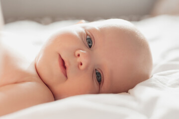 closeup portrait of a blue-eyed newborn baby lying on his back on a white sheet. happy carefree infa