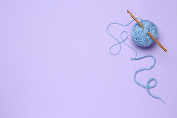 Wall Mural - Clew of light blue knitting thread and crochet hook on violet background, top view. Space for text