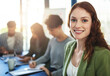 © Delmaine Donson/peopleimages.com - This company is built on excellence. Portrait of a young businesswoman sitting in an office with colleagues in the background.