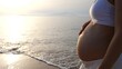 © Sia - A pregnant woman walks along the beach in the rays of the soft setting sun. Stroking his big tummy with a baby inside. A woman before the birth of a baby spends time in fresh air.