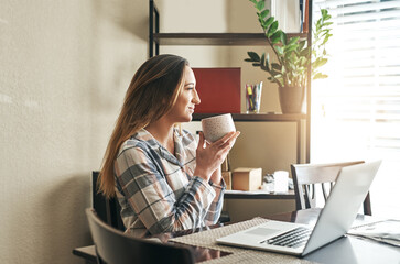 Canvas Print - Coffee first then Ill do some browsing. Cropped shot of a young woman drinking coffee and using a laptop in the morning at home.