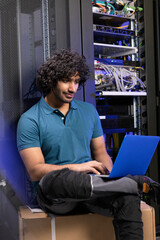 Computer programmer using laptop sitting on box in server room