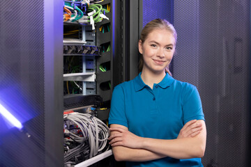 Blond IT trainee standing with arms crossed in server room at industry