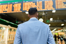 Businessman Standing In Front Of Departure Board At Train Station