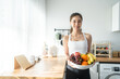 © Kawee - Asian attractive active woman holding bowl of fruit in kitchen at home.