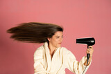 Beautiful smiling woman drying her long hair with electric fan