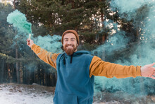 Happy Young Man Holding Blue Distress Flare In Forest