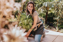 Smiling Gardener Kneeling By Potted Plant In Garden