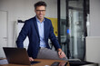© Westend61 - Happy businessman wearing eyeglasses sitting with laptop on desk in office