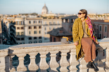 Wall Mural - Woman enjoying beautiful morning cityscape of Rome, sitting on the top of famous Spanish steps. Old fashioned woman wearing coat with colorful shawl in hair. Concept of italian lifestyle and travel