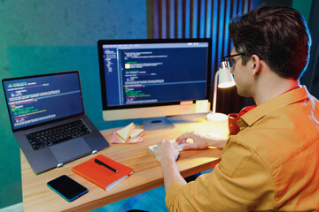 Back rear side view young smart data scientist software engineer IT specialist programmer man wearing shirt work at home writing programming code script on laptop pc computer Game development concept