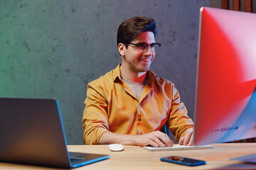 Young fun successful employee programmer IT specialist business man in casual shirt sit work at office desk with pc laptop desktop computer writing code Achievement career program development concept.