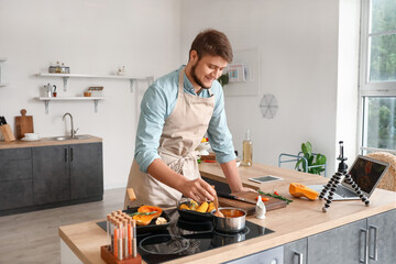 Wall Mural - Young man cooking vegetables while following video tutorial in kitchen