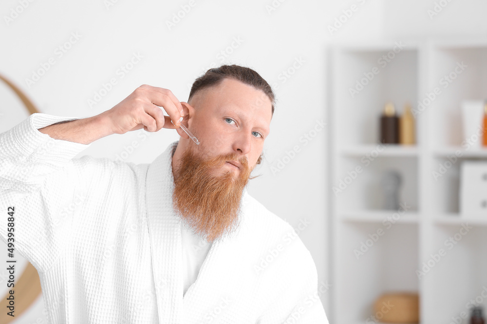 Handsome man with serum taking care of his beard at home