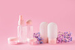 Set of empty travel cosmetic bottles and flowers on pink background