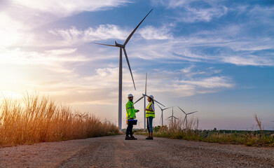 Engineer wearing uniform ,helmet hold document inspection work in wind turbine farms rotation to generate electricity energy. Green ecological power energy generation wind sustainable energy concept.