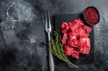 Raw diced red beef meat for Goulash on marble board. Black background. Top view. Copy space