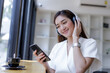 © SHUTTER DIN - freelance business woman sitting by the glass window and streaming listening to music from mobile phone to white wireless 5.0 headphone in the coffee shop,
